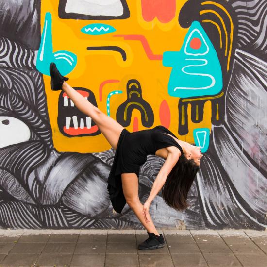 Eine Frau nimmt vor einer bunt bemalten Wand eine tänzerische Pose ein.