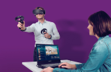 Vor einem lilafarbenen Hintergrund steht ein Mann mit VR-Brille und weiteren Utensilien in der Hand. Im Vordergrund sitzt eine Frau an einem Laptop und betreut die Situation.