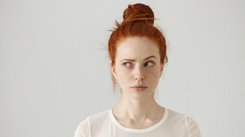 Frau mit weißem Oberteil und roten Haaren, die skeptisch guckt.