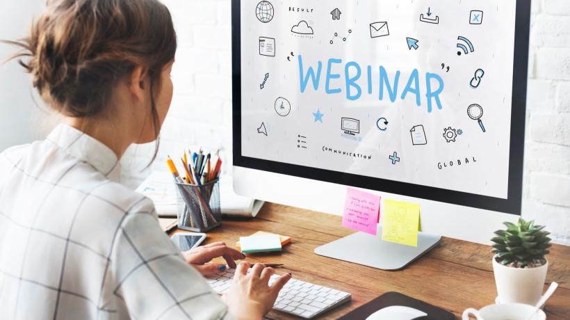 Eine Frau sitzt am PC, auf dem Desktop sieht man groß das Wort WEBINAR