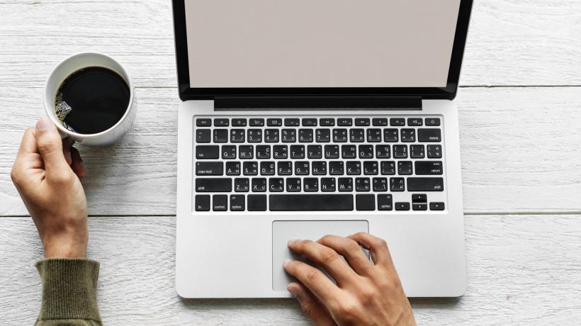 Person schreibt an Computer mit Kaffee