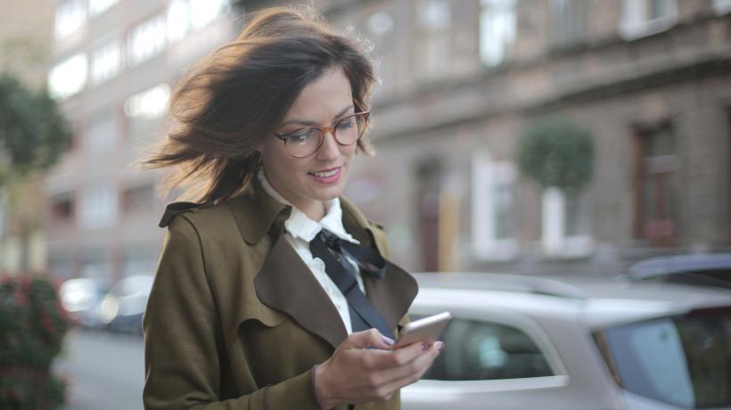 Frau läuft auf dem Bürgersteig und schaut dabei auf ihr Handy.