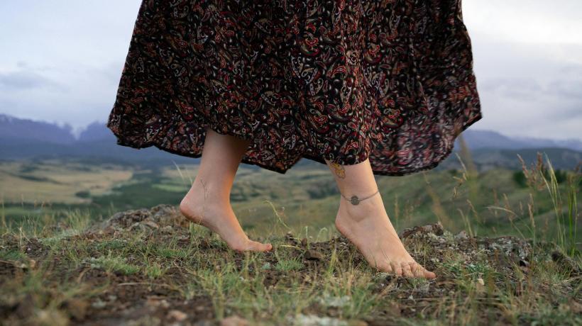 Man sieht die baren Füße einer Frau im Kleid, die über eine Grasfläche läuft.