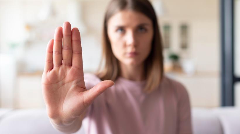 Eine junge Frau hält ihre Handfläche abwehrend vor sich in die Kamera.