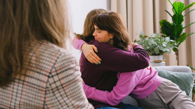 Drei Frauen in einem Beratungsraum, zwei Frauen geben sich eine Umarmung.