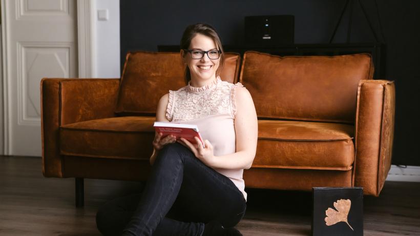 Bild von Cornelia Fiechtl, die auf dem Fußboden sitzt und sich an einer Couch anlehnt.