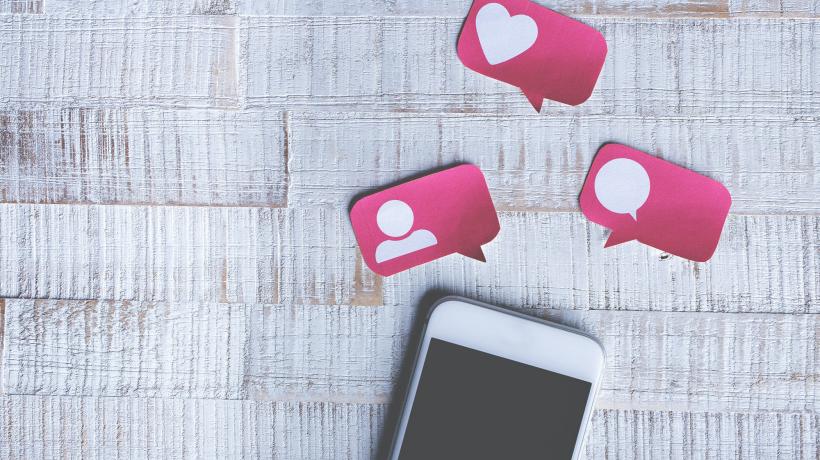 Smartphone mit kleinen pinken Sprechblasen darüber liegt auf einem Tisch.