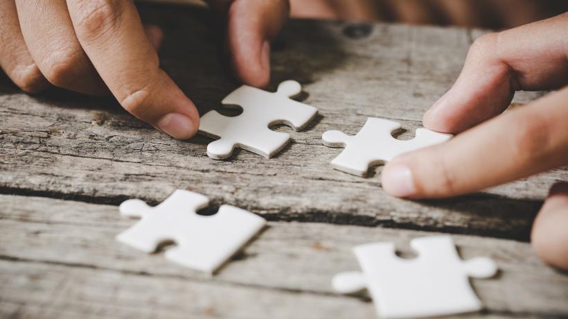 Zwei Hände, die vier Puzzleteile auf einer Holzfläche zusammenlegen