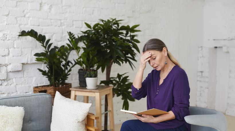 Eine Frau sitzt auf einem Sofa und liest, im Hintergrund ein Raum mit Pflanzen und weißen Wänden
