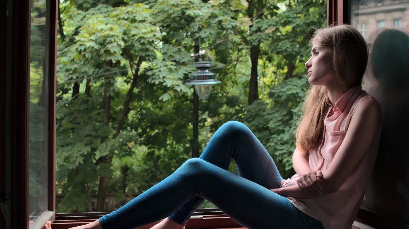 Traurige junge Frau sitzt an einem offenen Fenster