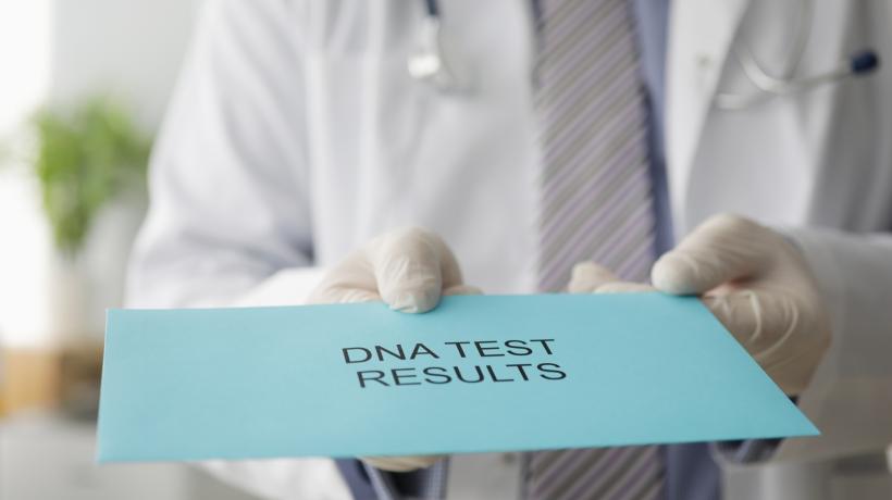 Eine Person in medizinischer Kleidung hält einen blauen Umschlag mit DNA TEST RESULTS in der Hand.