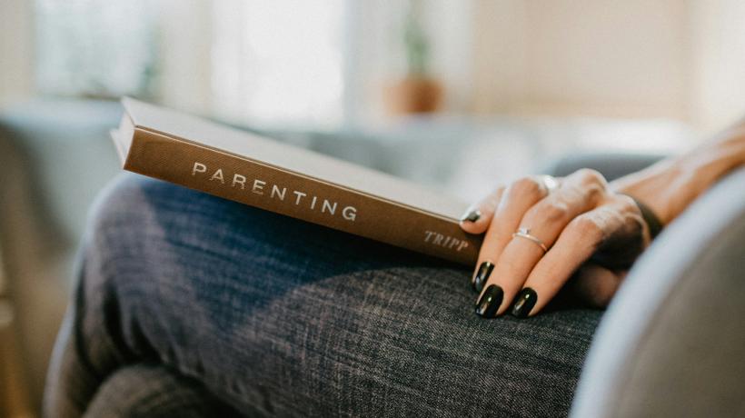 Man sieht ein Buch mit dem Titel Parenting auf dem Schoß einer Person liegen.