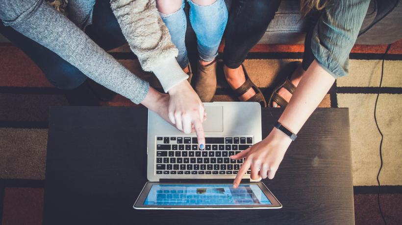 Drei Frauen, von oben fotografiert, sitzen vor einem Laptop und zeigen auf den Bildschirm.