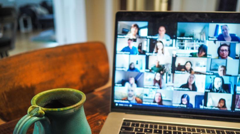 Laptop auf Schreibtisch mit Tasse daneben. Auf dem Bildschirm sieht man diverse Bilder aus einem Videochat.