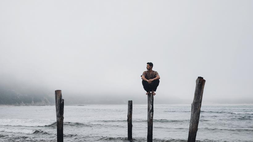 Mann, der am Meer auf einem von vier Pfosten sitzt