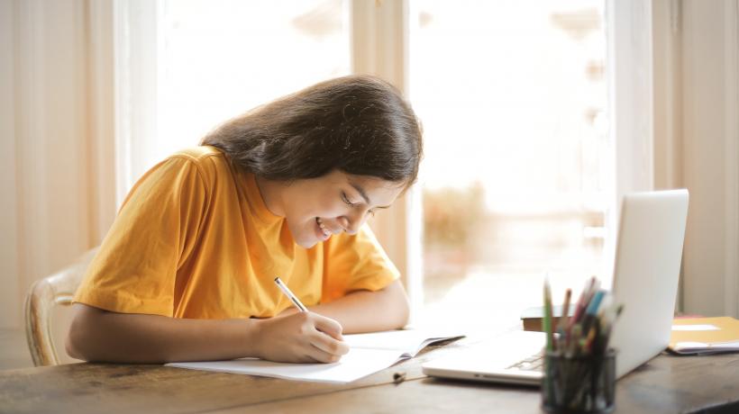 Studentin sitzt schreibend am Tisch