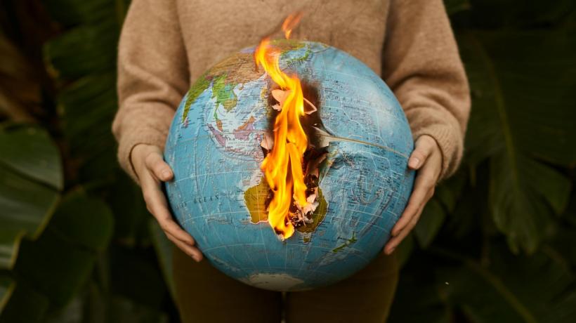 Eine Person hält einen Globus in der Hand, der in Flammen steht.