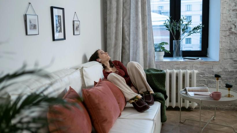 Eine Frau sitzt müde auf dem Sofa und schaut an die Decke.