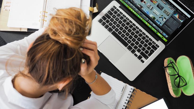 Frau sitzt erschöpft, den Kopf an den Händen gestützt, am Laptop