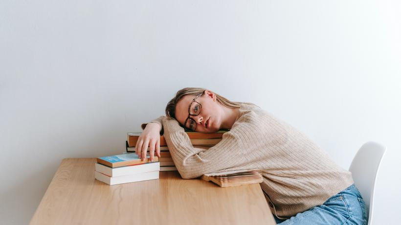 Frau sitzt müde am Tisch vor ihren Büchern