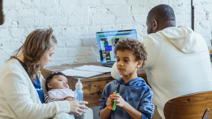 Mann im Hintergrund vor Laptop, vorne seine Familie