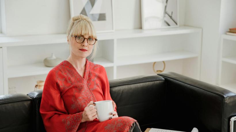 Eine Frau sitzt auf einem schwarzen Sofa und hat eine Teetasse in der Hand.
