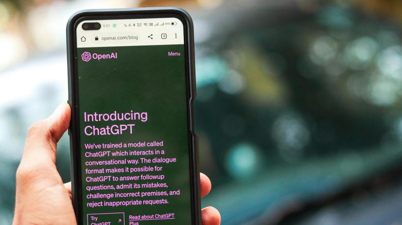 Man sieht ein Smartphone in einer Hand, auf dem das Interface von ChatGPT dargestellt ist.
