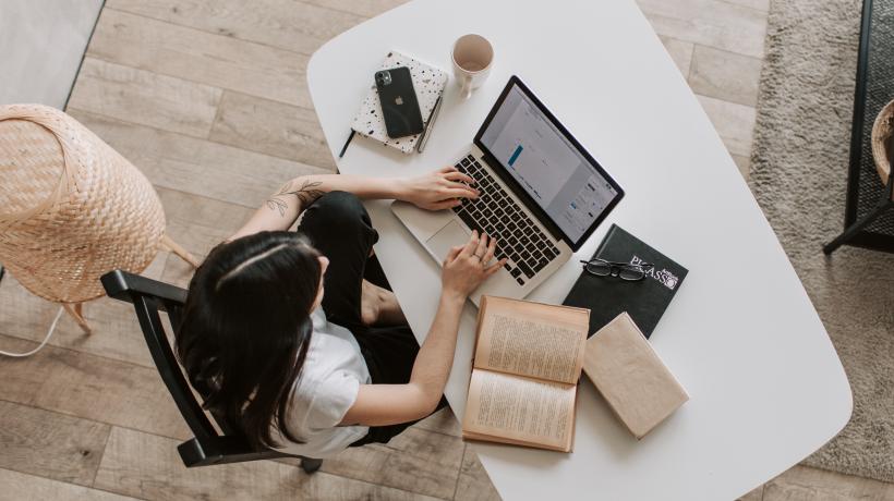 Frau am Schreibtisch mit Laptop und Büchern von oben