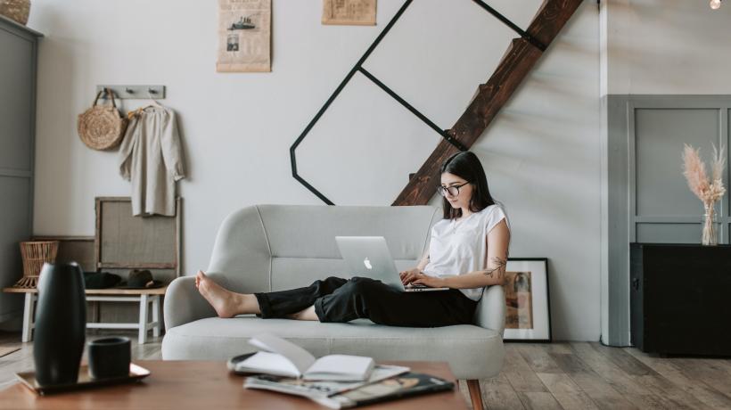 Frau sitzt mit Laptop auf Sofa