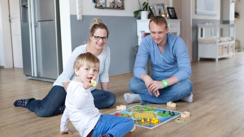 Mutter, Vater und Sohn sitzen auf dem Boden uns spielen ein Brettspiel.