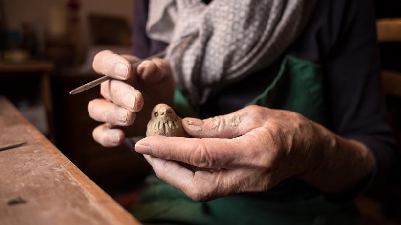 Hände einer älteren Person, die einen kleinen Vogel aus Ton halten.