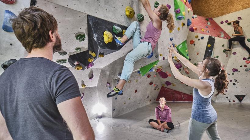 Eine Frau klettert, eine Frau sichert sie und ein Mann guckt zu