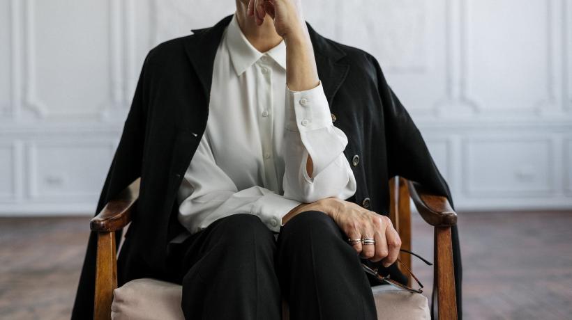 Eine Frau, deren Gesicht nur halb zu sehen ist, hat einen Arm vor sich verschränkt und hält sich mit dem anderen die Hand ans Kinn.