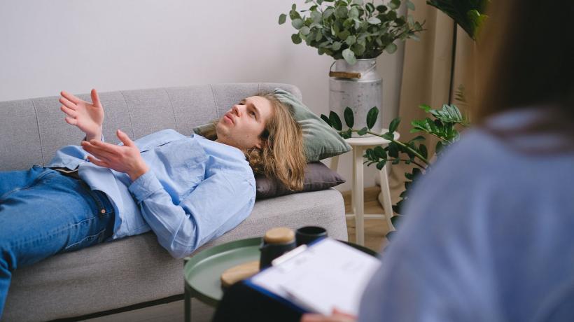 Ein junger Mann liegt auf der Couch und schildert einer Therapeutin etwas, die sich Notizen macht.