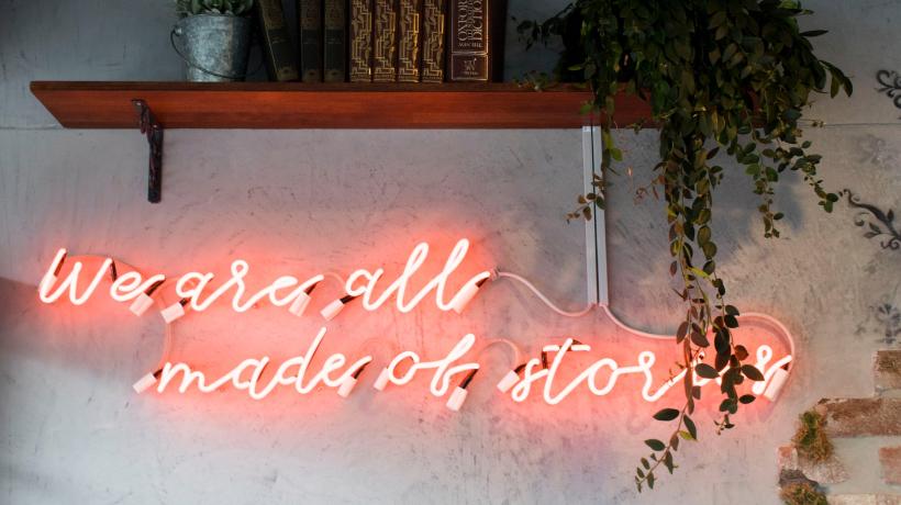 An einer Wand sind leuchtende Buchstaben befestigt, die den Satz "We are all made of stories" ergeben.