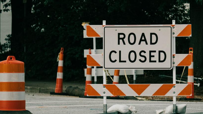 Straßenabsperrung mit orange-weißen Planken und einem weißen Schild, auf dem "ROAD CLOSED" geschrieben steht