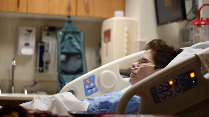 Frau liegt in Krankenhausbett und bekommt Sauerstoff.