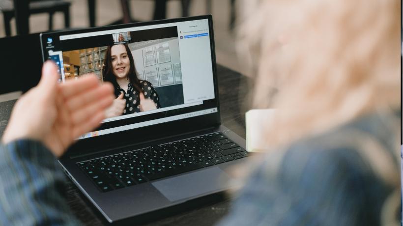 Frau sitzt vor Laptop auf dessen Bildschirm im Videochat eine andere Frau zu sehen ist.