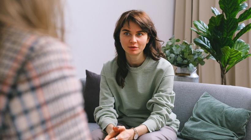 Junge Frau spricht mit einer Therapeutin, die nurr von hinten zu sehen ist.