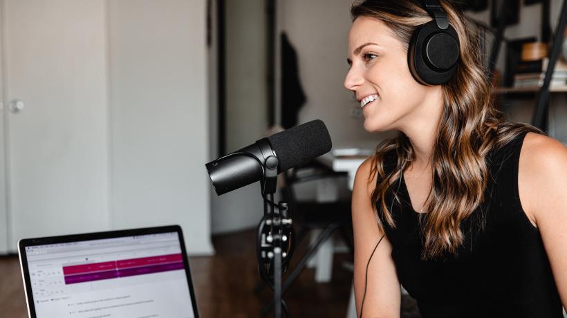 Frau sitzt vor Mikrofon und Laptop mit Kopfhörern und nimmt einen Podcast auf.