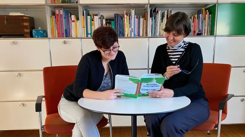 Zwei Erwachsene Frauen schauen sich gemeinsam ein Bilderbuch an.
