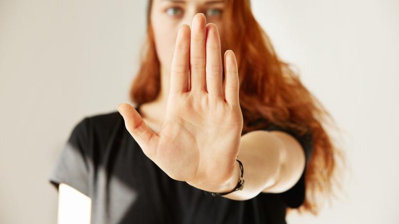 Eine Frau hält mit ausgestrecktem Arm ihre Handfläche auf Brusthöhe nach vorn in die Kamera (Stopp-Geste).